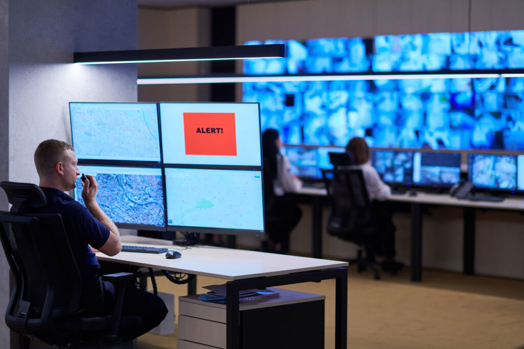 A person sitting in a control room, looking at four computer screens on which 