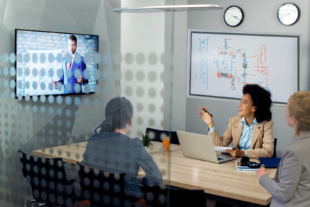 Three people sitting in a Huddle room, where a wall screen is showing an image - using Kramer Huddle Room solutions