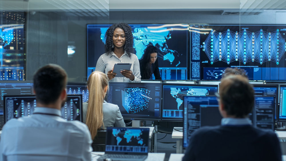 People working at a control room, with a woman displayed on the screen, a place where NETGEAR and Kramer's is installed to provide AVoIP deployment