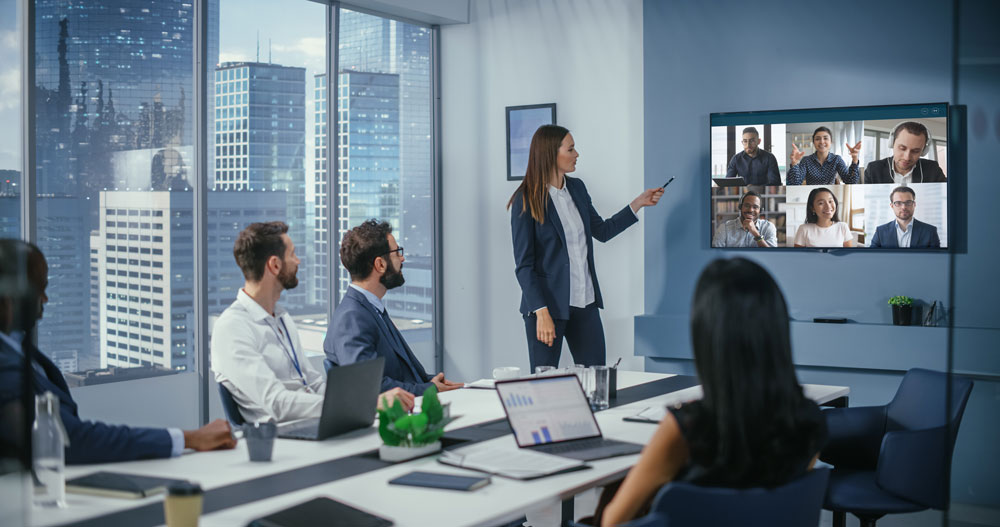 People sitting in a hybrid meeting room, looking at the wall screen, using Kramer and Sennheiser sound solutions