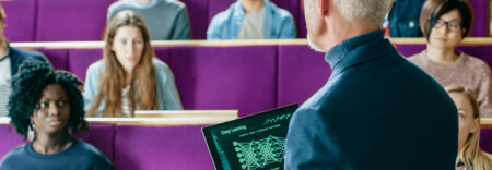 A professor standing in an auditorium, holding a laptop, using Kramer's AV