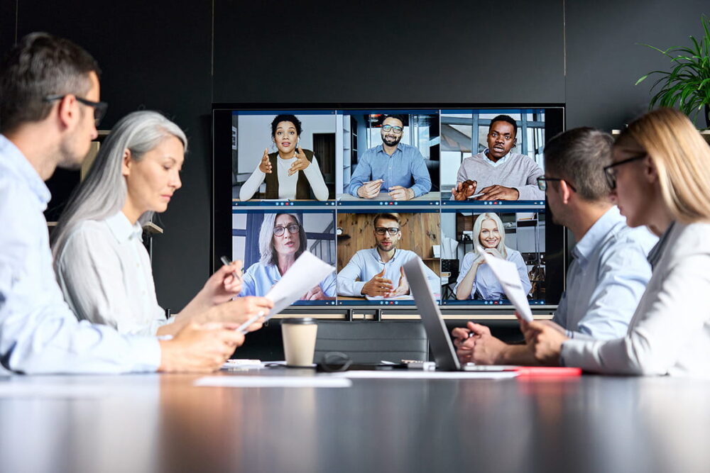 People sitting in a meeting room, while people appear on the wall screen, using Kramer AV soultions