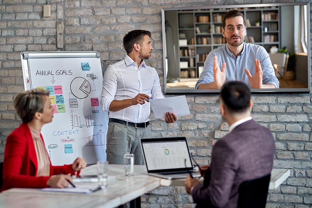 People sitting in a hybrid meeting room, looking at the wall screen, using Kramer and Sennheiser sound solutions