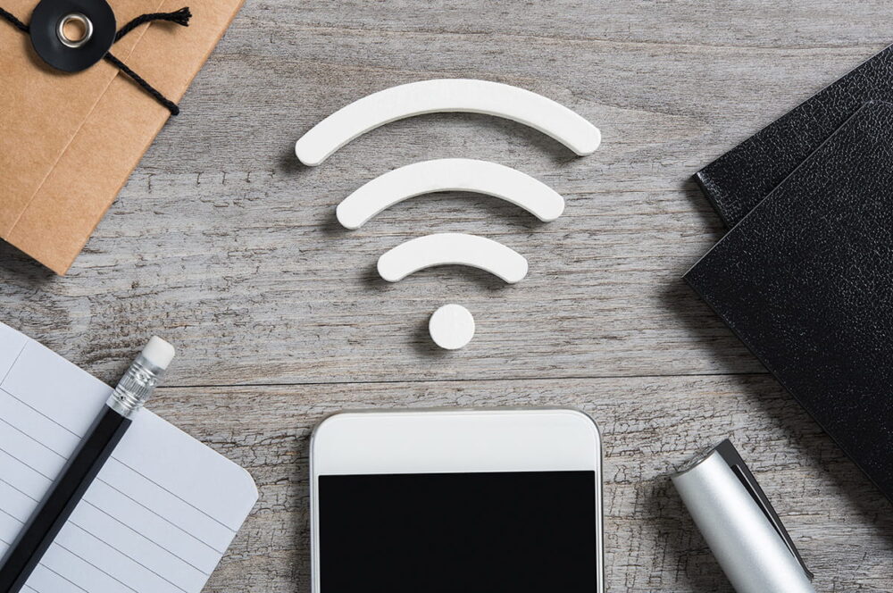 A table with a notebook, pencil, and a mobile phone from which there's a WiFi symbol coming out