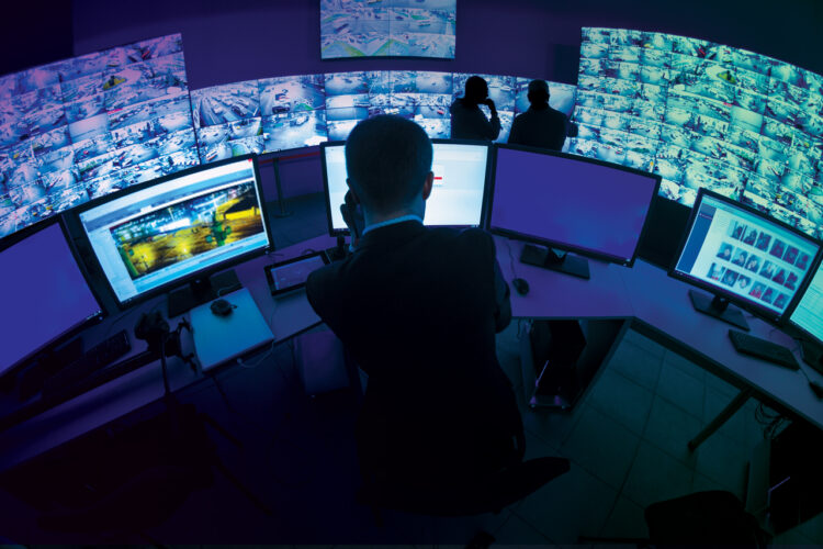 People photographed from the back, sitting in a control, dark room in front of multiple screens, using Kramer's Control solution
