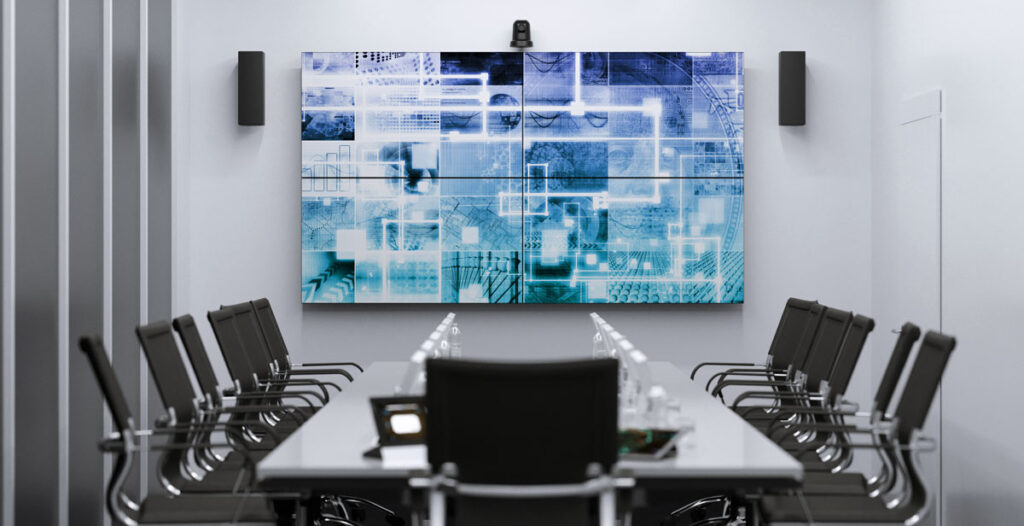 A large meeting room, chairs around a table, and a mounted wall screen 