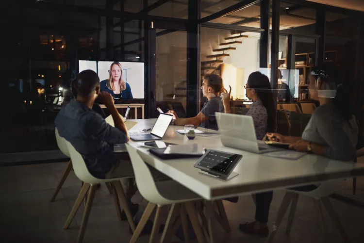 People sitting in a meeting space, looking at a screen with a remote participant on it