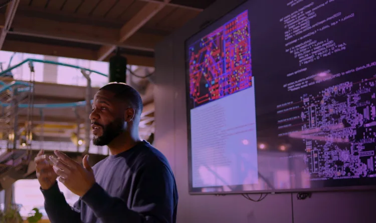 A man standing, teaching. On his back there are several wall screens, powered by KDS-17