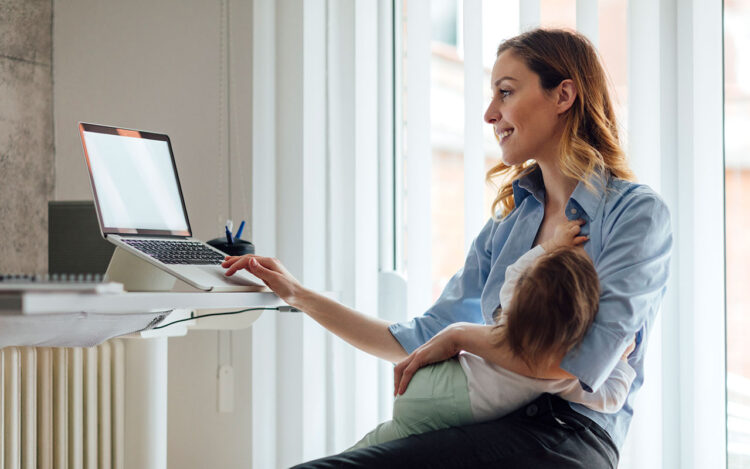 A woman holding her child, smiling at the computer during a meeting